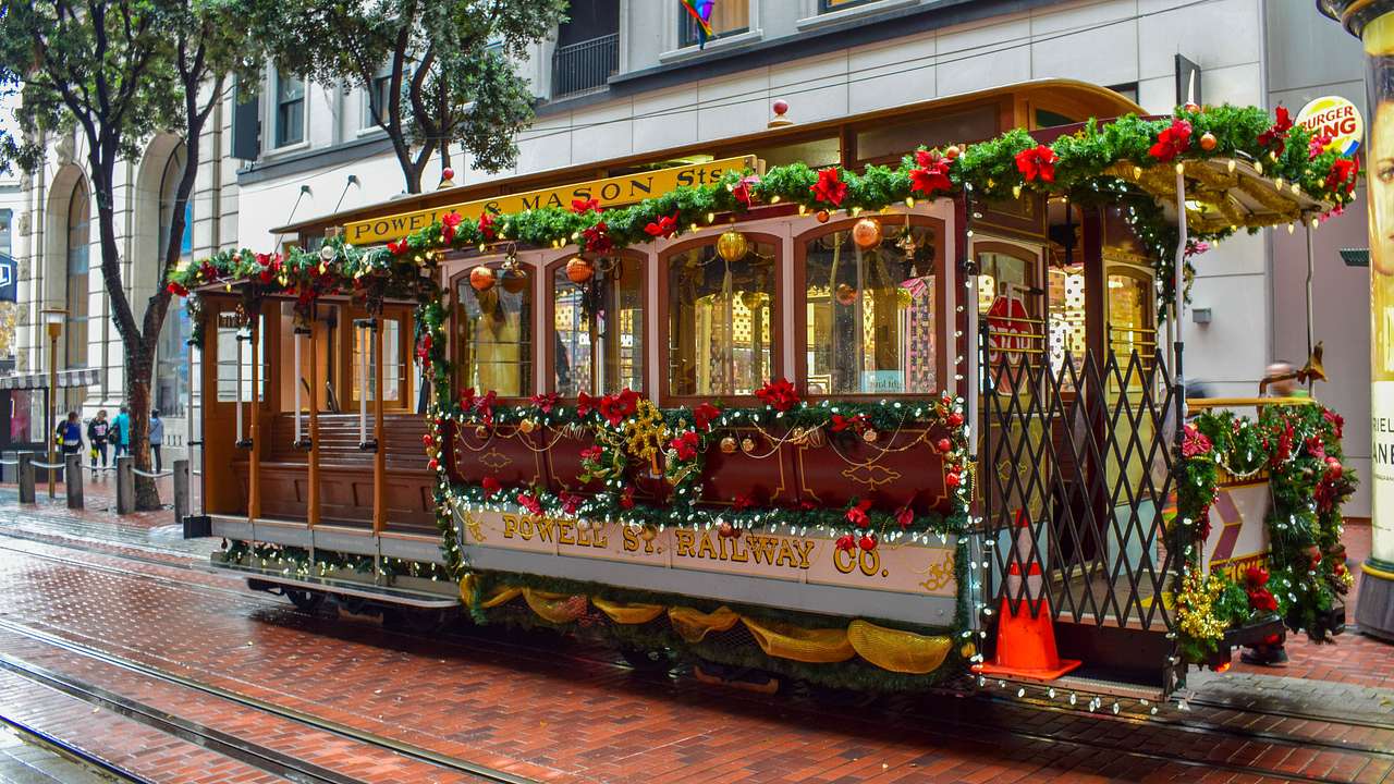 A brown streetcar decorated with holiday garlands, lights, and bows