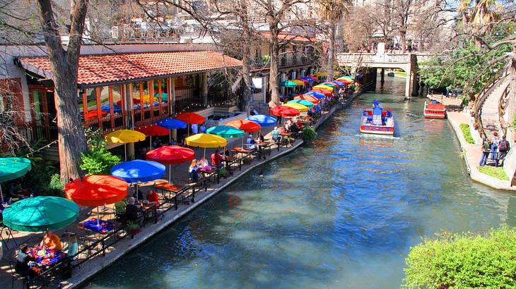 Many multi-colored umbrellas on a patio with a body of water beside it on a sunny day