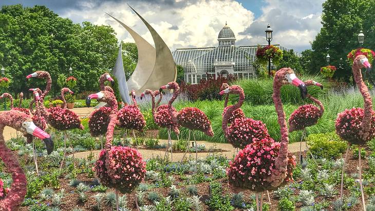 Flamingos made from flowers next to a sculpture and conservatory on a cloudy day