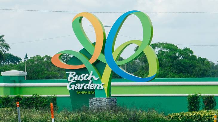A sign with the words "Busch Gardens" next to grass and trees