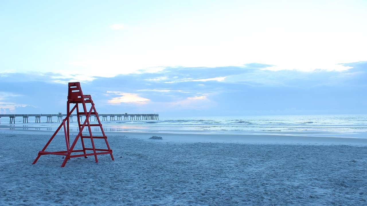 A red lifeguard seat alongside the sea and a jetty in the distance
