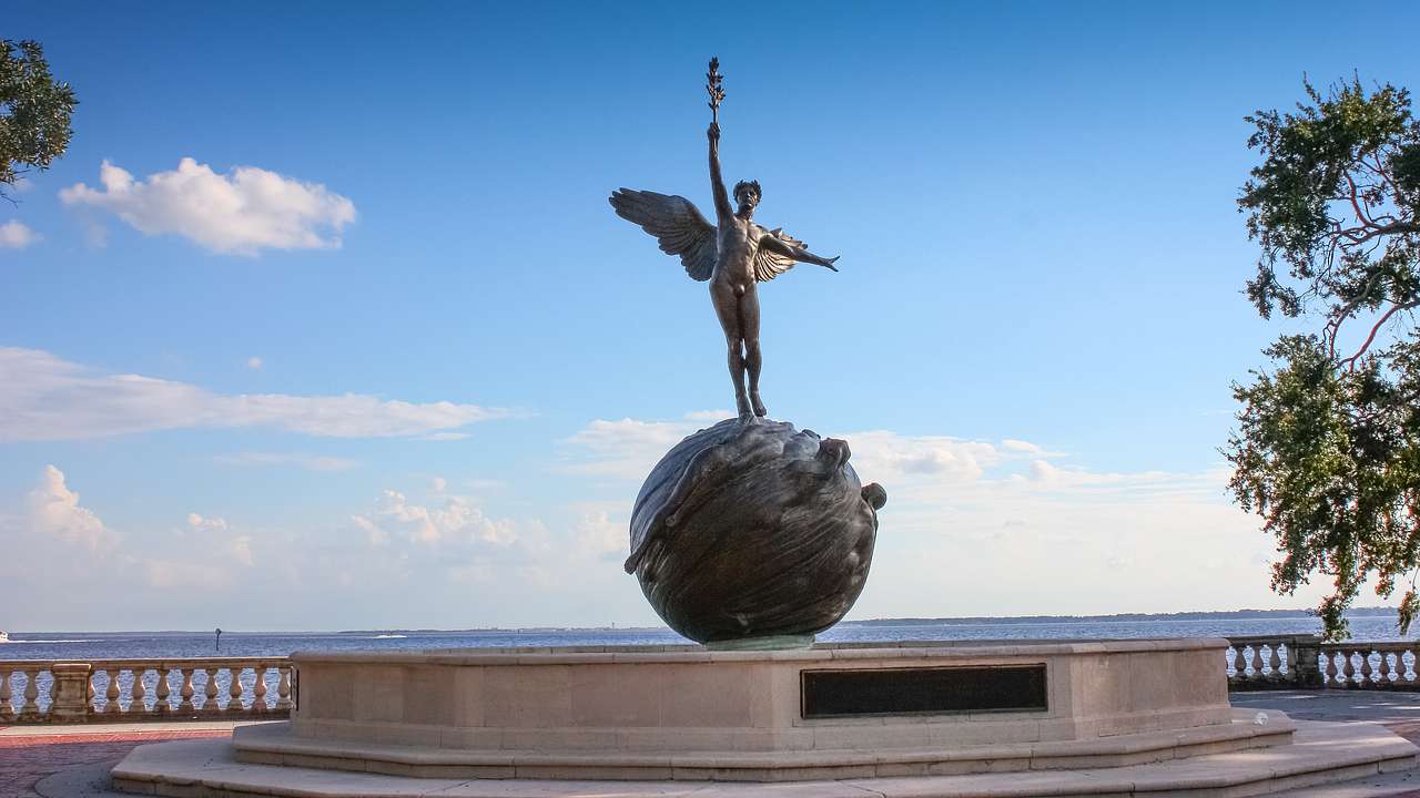 A winged statue on an orb on a concrete pedestal next to a blue sky with some clouds