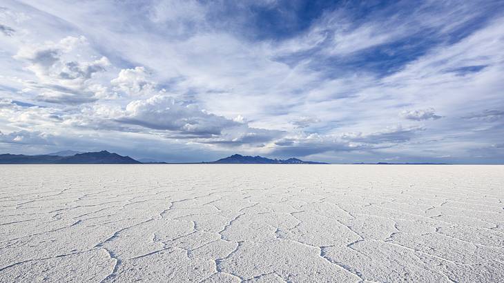 White salt flats with mountains in the distance under a cloudy sky