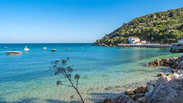 Turquoise ocean water with boats on it and a hill and house in the background Turquoise ocean water with boats on it and a hill and house in the background