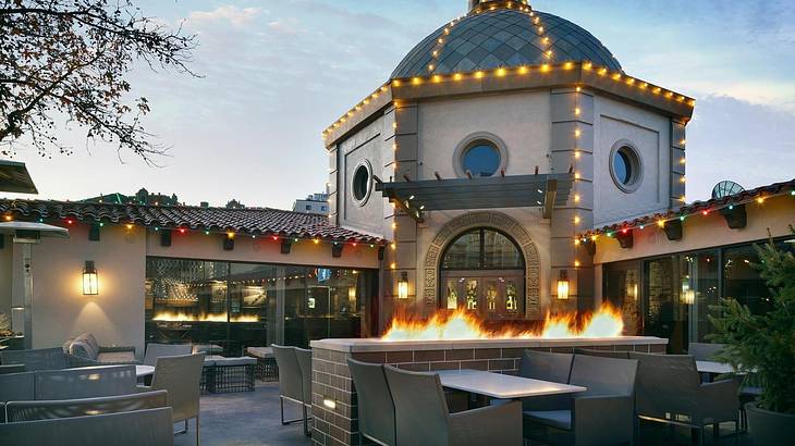 A patio with dining tables and fire pits and a building with a dome room and lights