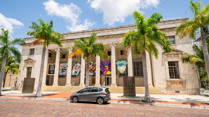 Palm trees in front of a neoclassical structure with artworks outside on a sunny day