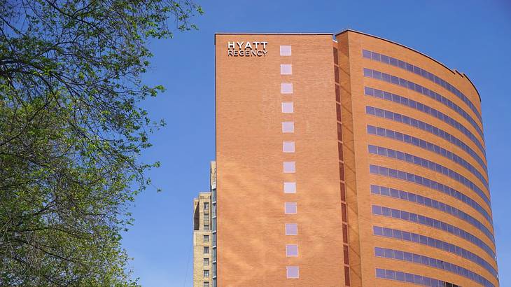 A tall red brick building with a "Hyatt Regency" sign next to trees and a blue sky