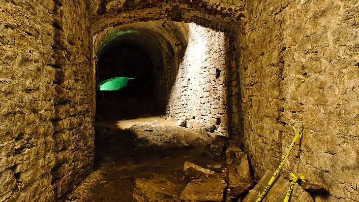 An underground stone tunnel with a green light in the distance