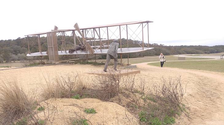 A statue of a man pushing an old airplane monument on a sandy area