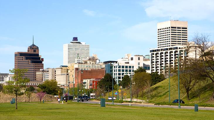 A green field next to a pathway with green posts and a background of tall buildings