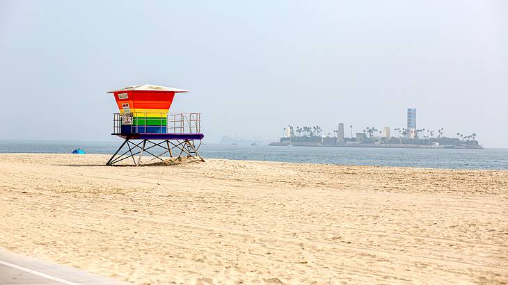 An empty beach with a colorful lifeguard tower and an isle in the distance