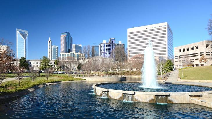 A water fountain in a park with city buildings next to it on a clear day