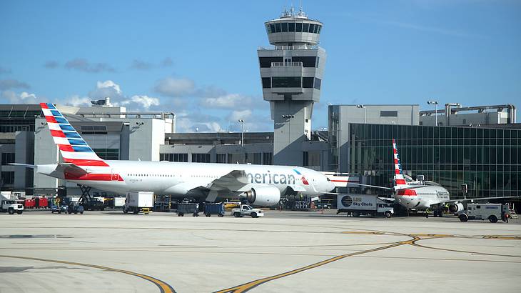 Two airplanes, one with a red striped tail, parked at an airport with a tower