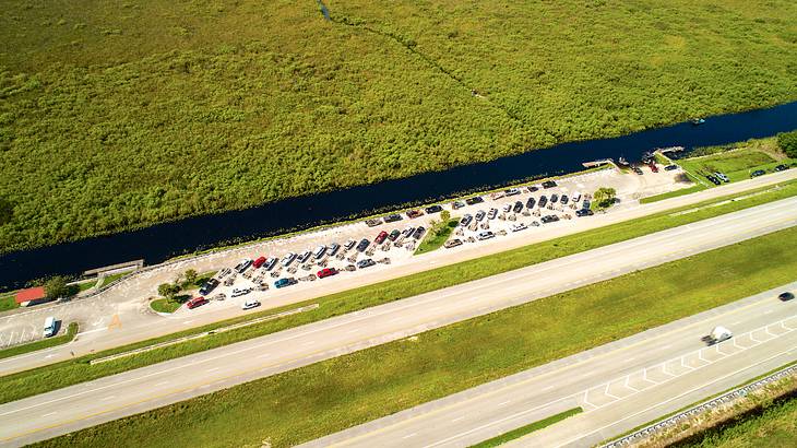 Rows of cars in a parking lot next to a narrow body of water lined with greenery