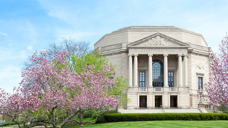 A stone building with columns next to green grass and cherry blossom trees A stone building with columns next to green grass and cherry blossom trees