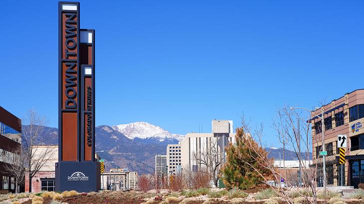 A "Downtown" sign in front of city buildings, with a snow-capped mountain at the back