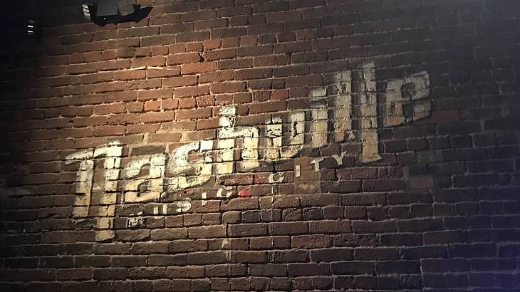 Dark brown brick wall with gold "Nashville Music City" sign painted on wall