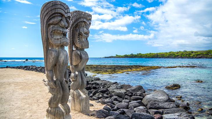 Tall wooden carvings on a rocky beach with a partly cloudy blue sky in the background