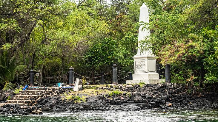 White monument surrounded by trees and facing a body of water