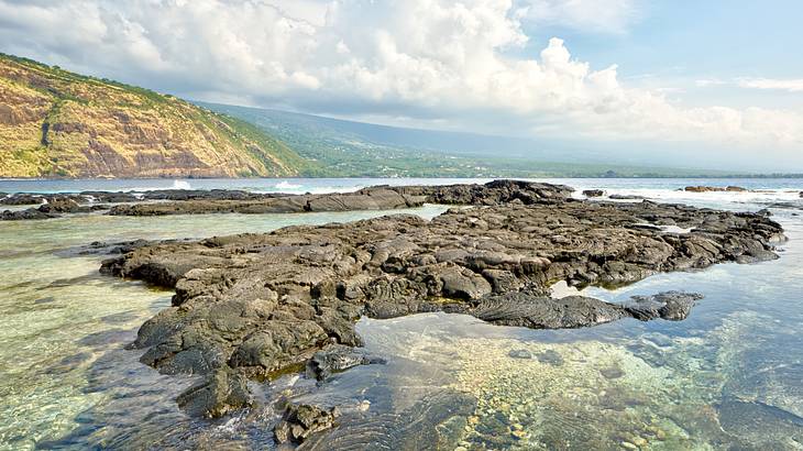 Looking out over water and rocks to hills and white fluffy clouds in the background