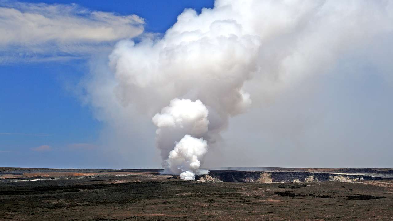 White smoke coming out of a vent in a black volcano against a blue sky