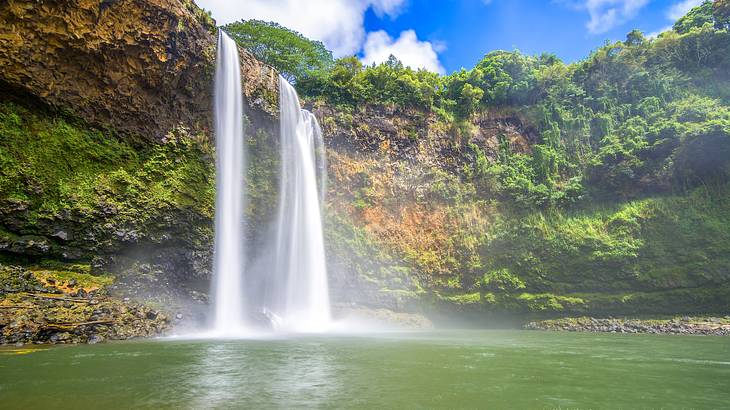 Twin waterfalls cascading down a rocky cliff into a pool below on a bright day