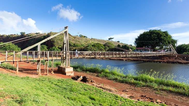 Wooden suspension bridge over a river with a blue sky and clouds in the background