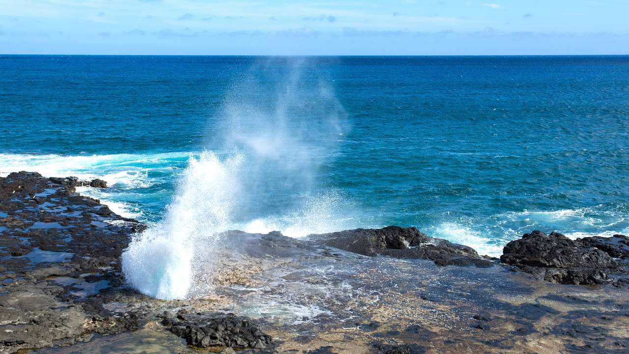 Water mist getting sprayed upwards out of a rock formation on the shore