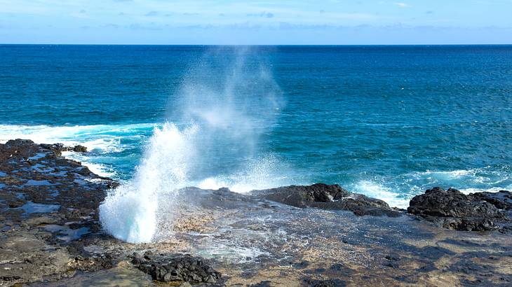 Water mist getting sprayed upwards out of a rock formation on the shore