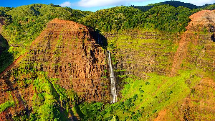 Aerial shot of a waterfall in the middle of a tropical canyon