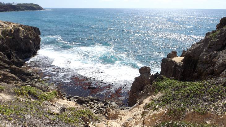 Waves crashing on a rocky shore leading to a rocky incline on a sunny day