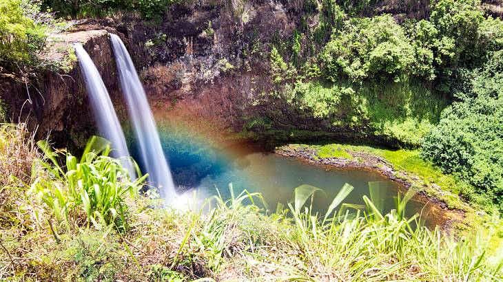 High-angle shot of a rainbow near the base of waterfalls in a tropical landscape