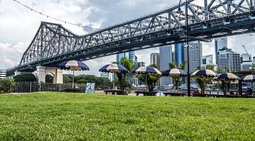 Tall buildings behind a bridge facing a grassy area with patio table umbrellas