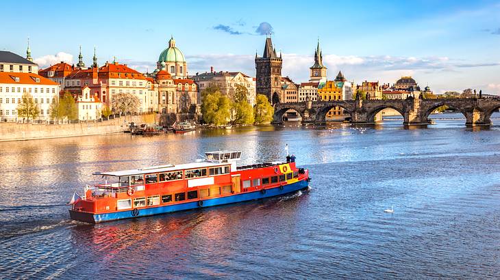 A river with a red and blue boat heading towards a bridge at the back