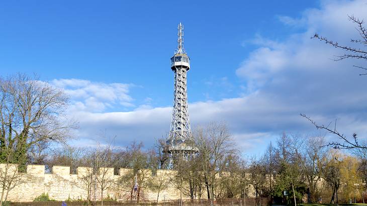 A tall grey tower overlooking bare trees on a green lawn from behind a wall