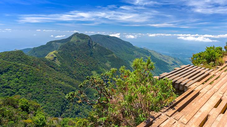 A wooden deck offering a top view of a green mountain under partially cloudy skies