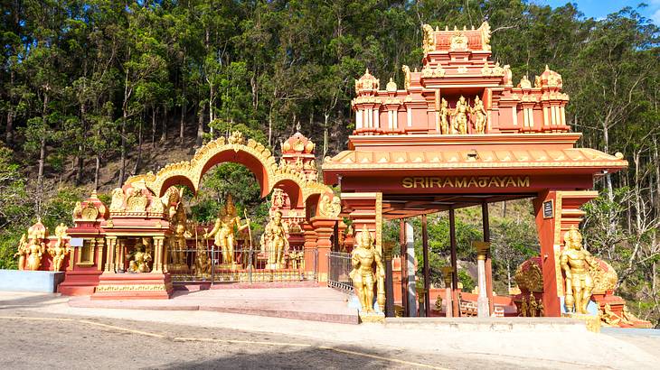 A brightly coloured peach temple with many statues and trees at the back