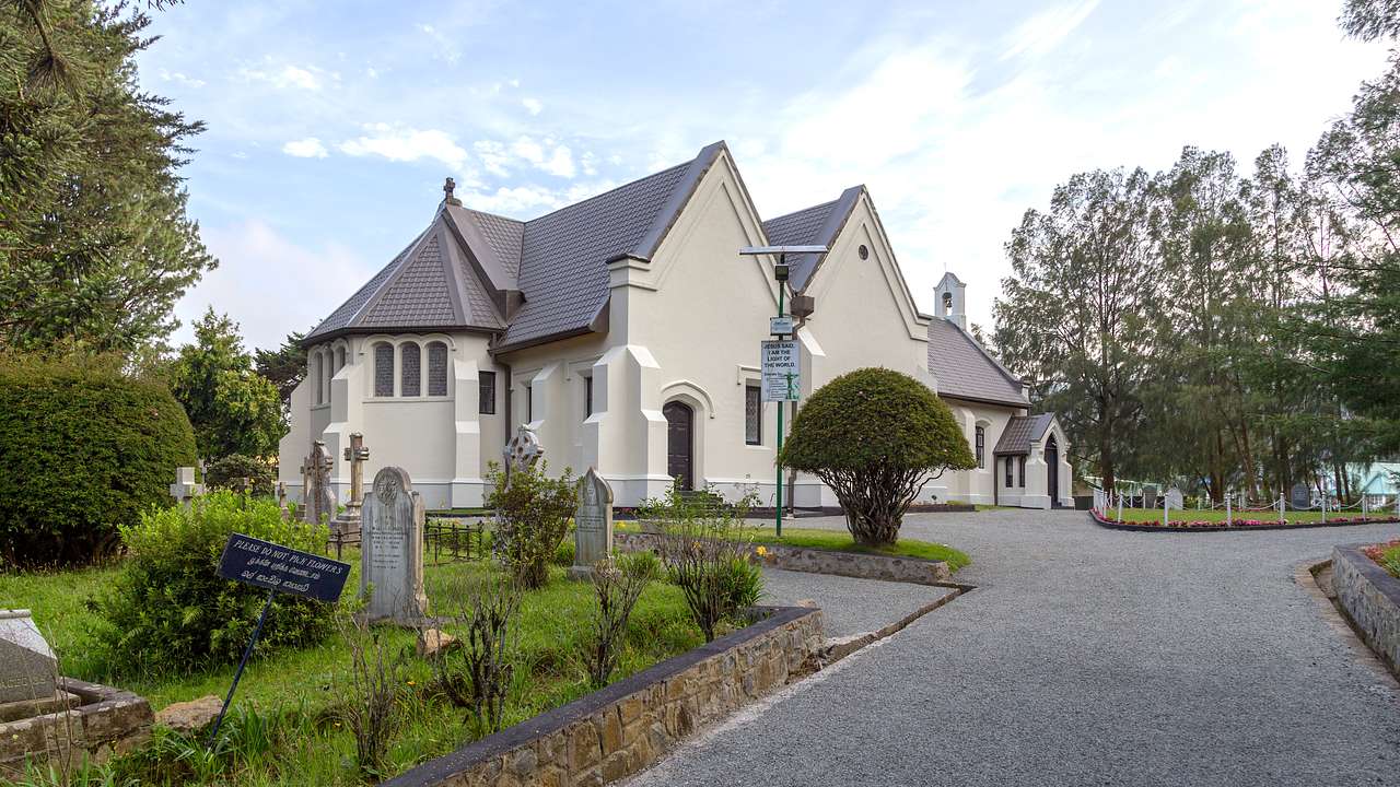 A picturesque church surrounded by a driveway, gravestones and greenery