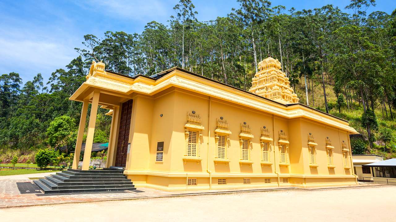 A long yellow temple from the side with a staircase and trees behind