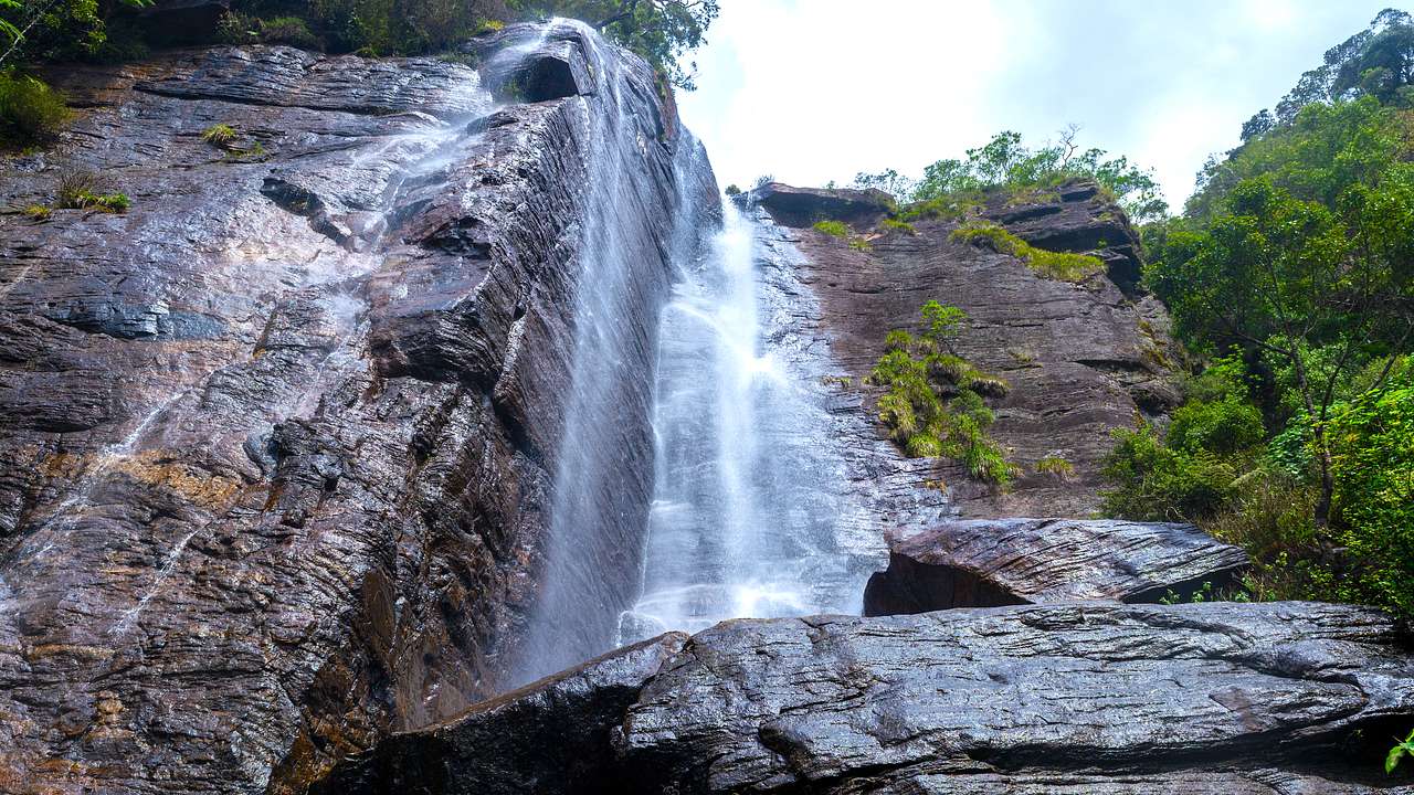 An up close shot of a cliffside waterfall cascading down rock with trees on the sides