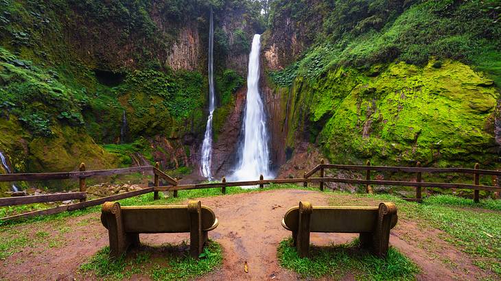 Two benches offering front-row views of two tall thin waterfalls