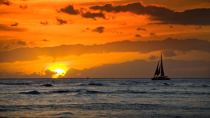Silhouette of a sailboat on the ocean with the golden sun setting in the background