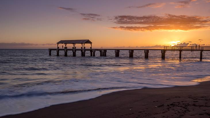 Sunset over a beach with a pier having a shed at one end in the background