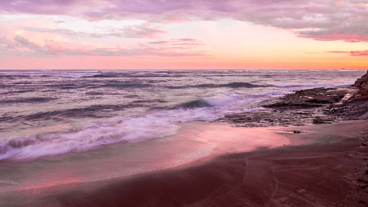 A beach glowing under a yellow and pink sky