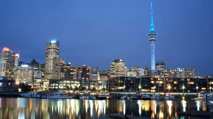 Lit-up tall city buildings with boats on the water in front at night