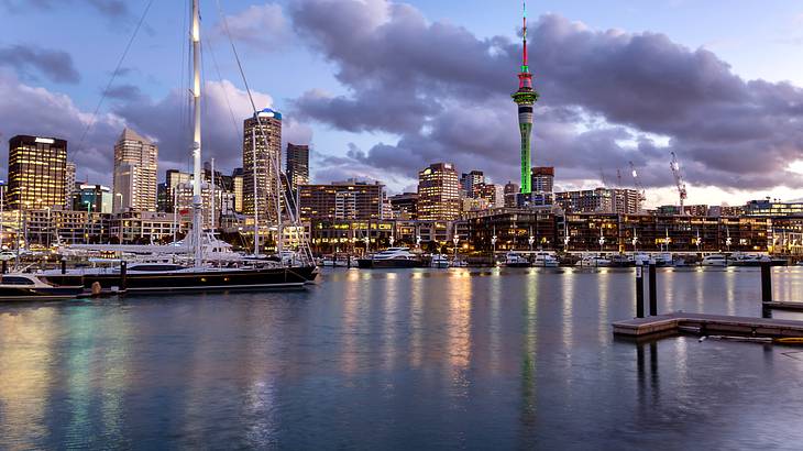 A harbour at sunset with a beautiful yacht and lit up city buildings at the back