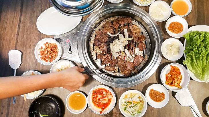 A barbecue grilling meat from above, surrounded by many small side dishes