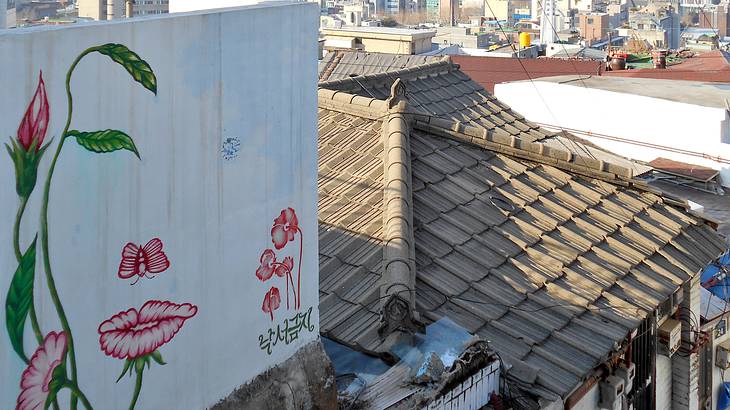 A mural of a face overlooking roofs of a village and a cityscape in the distance