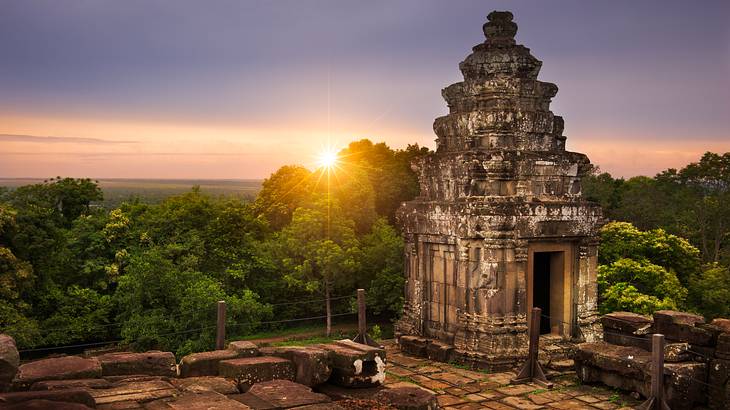 The sun setting behind green trees and an old temple