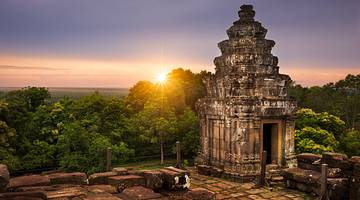 The sun setting behind green trees and an old temple